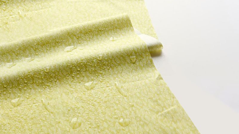 Close-up of yellow laminated film with water droplets on surface, showcasing water resistance.